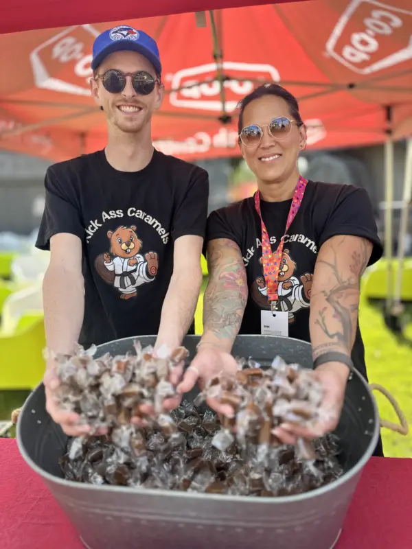 Two of the team holding a tub of caramels at a market